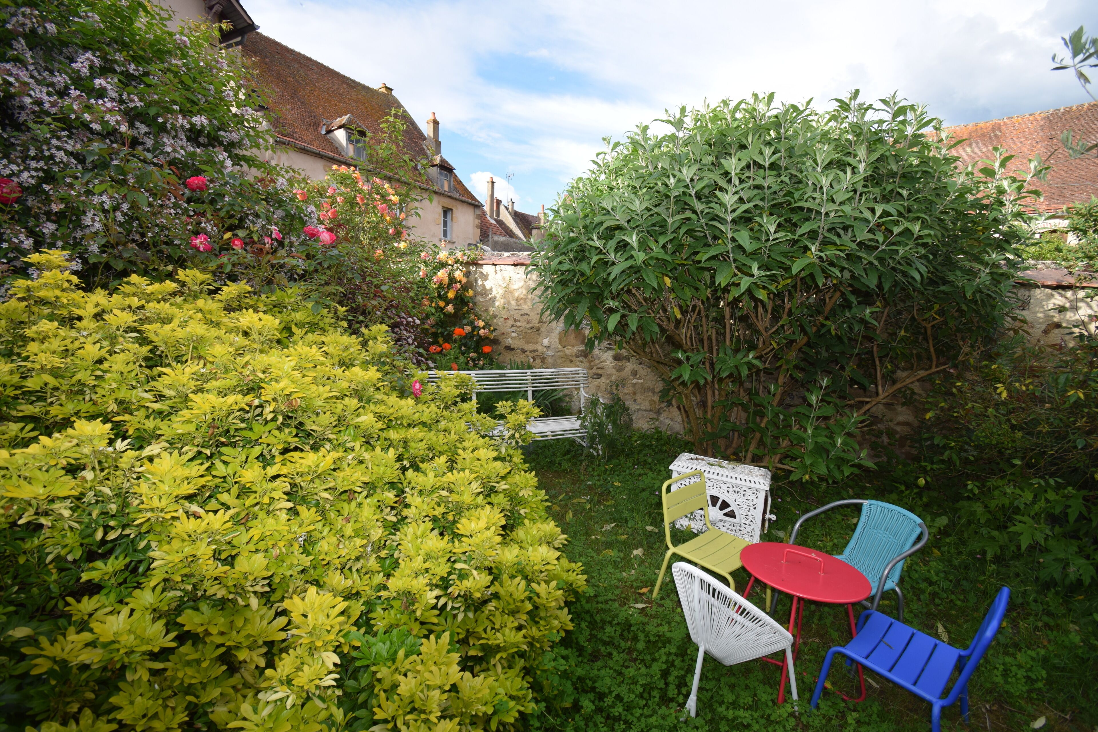 Un jardin agrémenté d’une petite table et de chaises, entouré d’une végétation luxuriante et de plantes en fleurs.