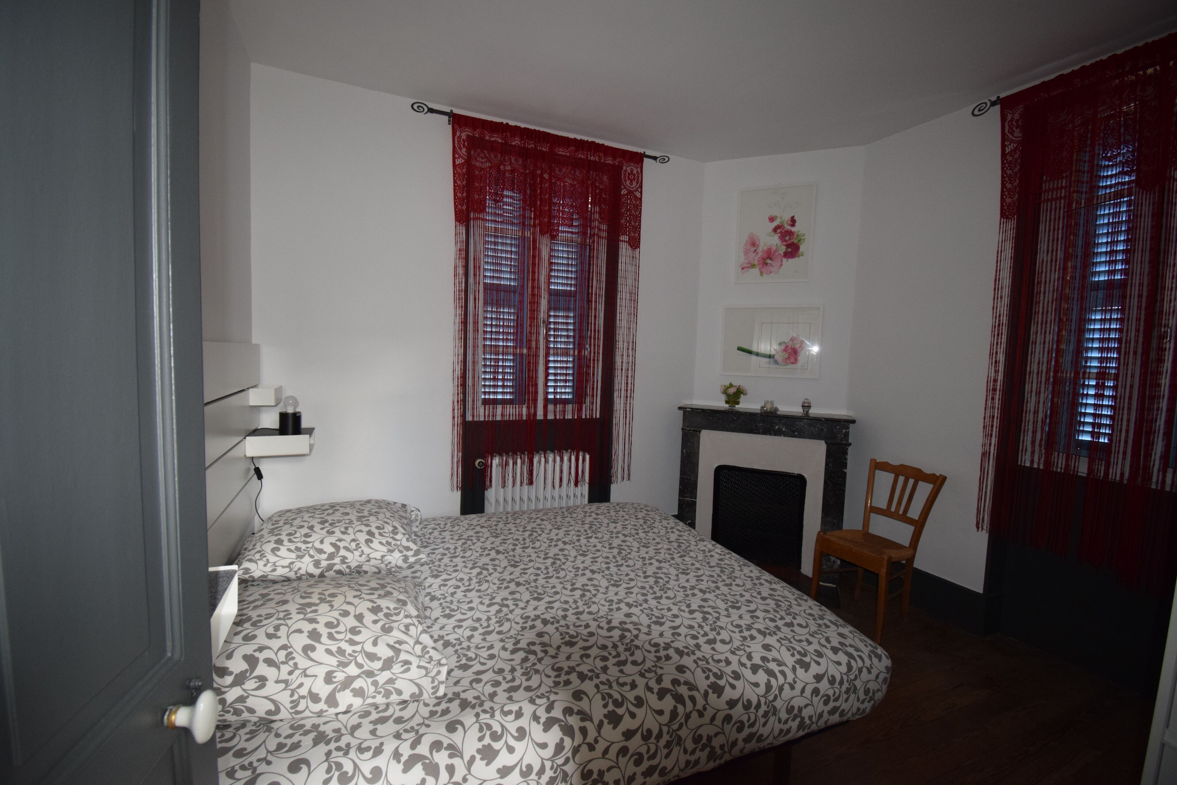 Een slaapkamer met een bed, een stoel, een open haard en rode gordijnen.
