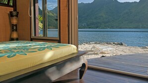 A room with a bed, a window, and a view of a beach and mountains.