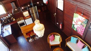 A wooden-floored room with a kitchen, two wicker sofas, a hanging light fixture, and a fire extinguisher.