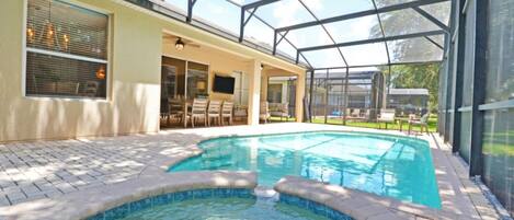 A swimming pool with a glass enclosure, patio furniture, and a view of the outdoors.