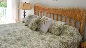 A bedroom with a bed, a ceiling fan, a wall-mounted decorative piece, and a view of greenery outside.