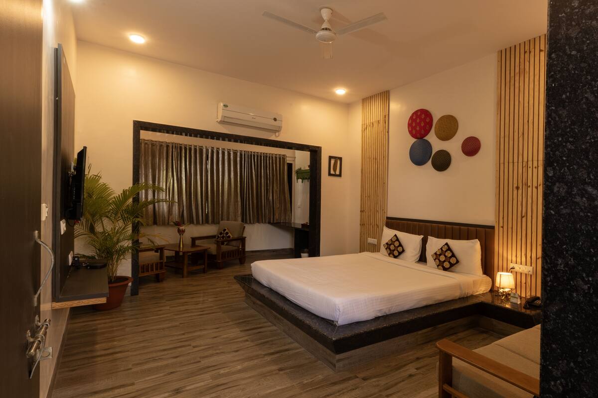 Habitación de hotel con cama, escritorio, silla, planta en maceta y aire acondicionado de pared.