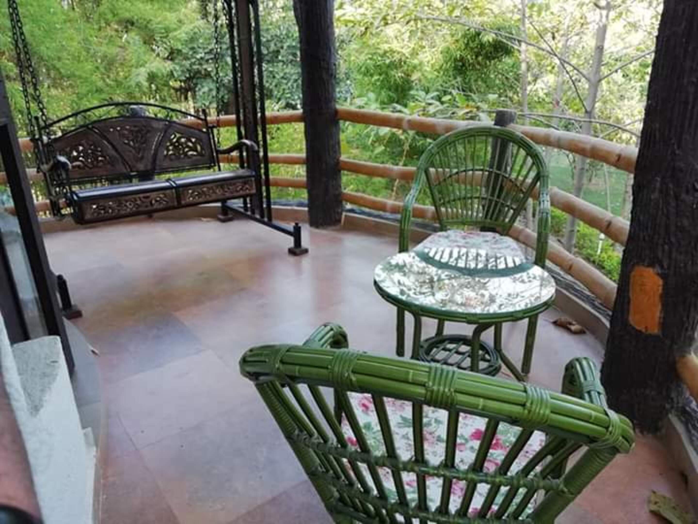 A covered outdoor area with a swing set, a table with chairs, and a view of greenery.