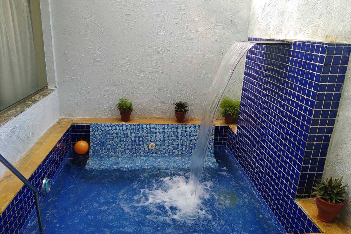 Una piscina interior pequeña con un borde de mosaicos azules, una fuente de agua y plantas en macetas.