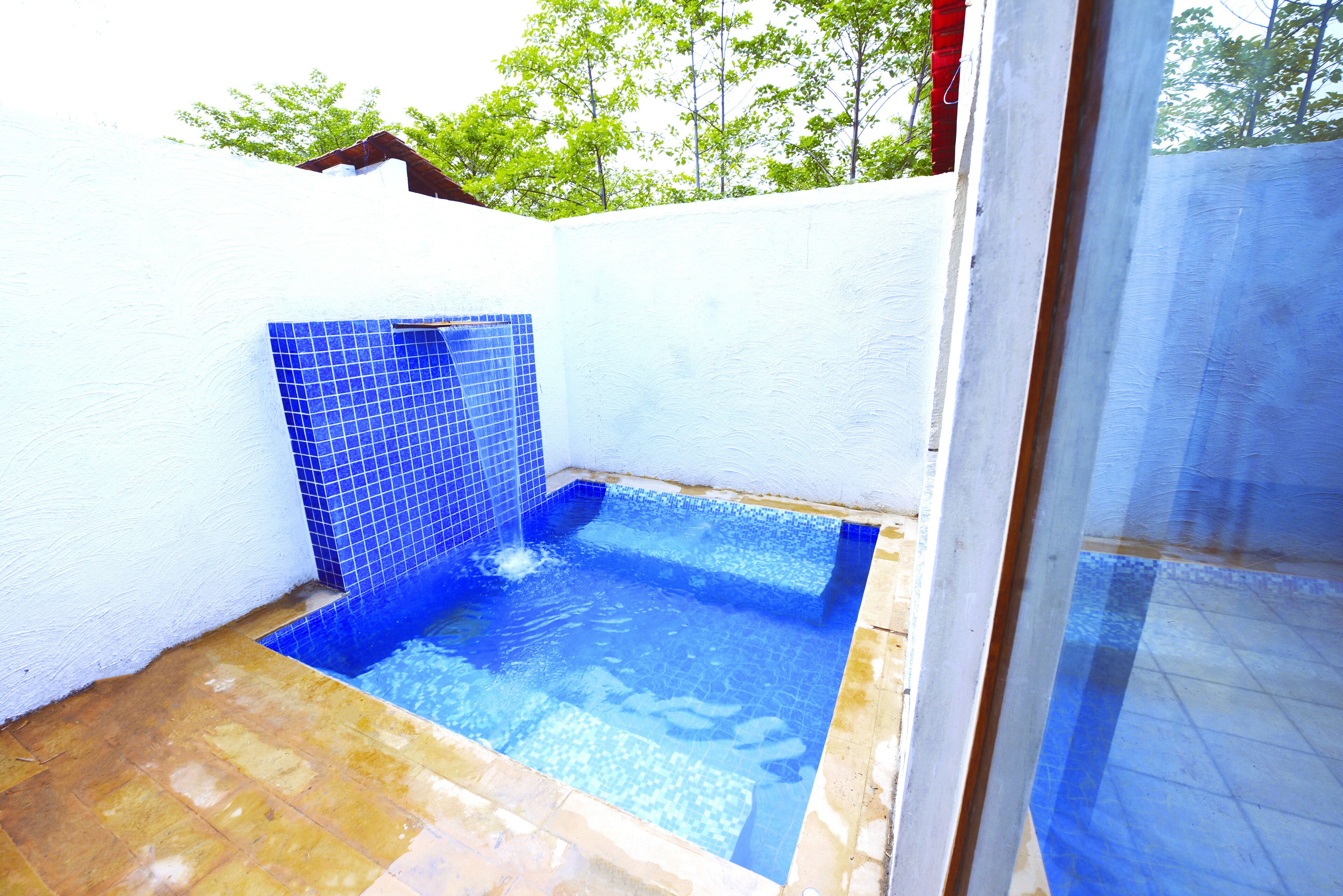Ein kleiner Pool im Freien mit blauen Fliesen, umgeben von einer weißen Mauer und einer Holzterrasse.