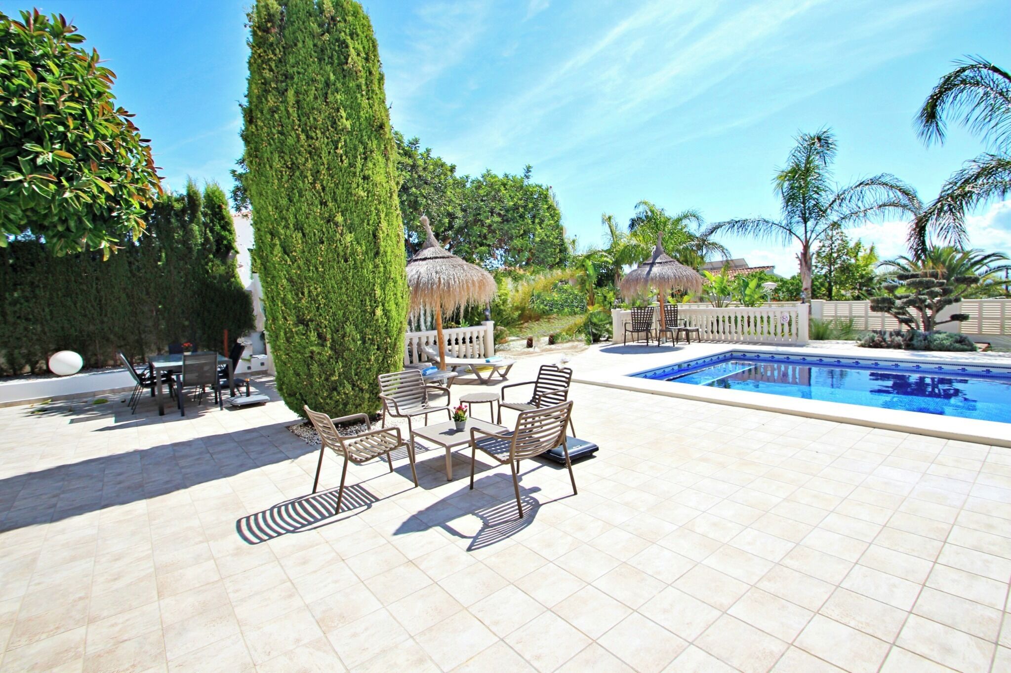 Ein Poolbereich mit gefliestem Deck, Liegestühlen und einer Struktur mit Reetdach.