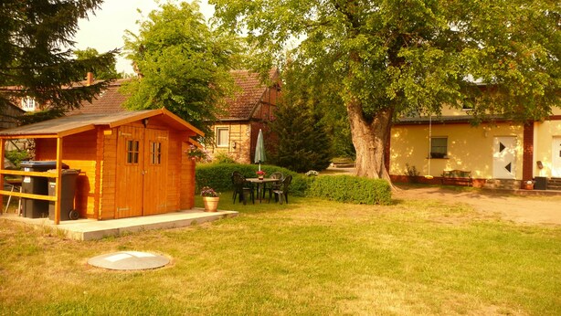 A wooden cabin with a small patio, a dining table with chairs, and a large tree in the background. - Beautiful apartment in the Müritz National Park to relax and unwind or active holidays. (Federow)