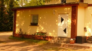 A small building with a white door and window, a bench outside, and a brick wall. - Beautiful apartment in the Müritz National Park to relax and unwind or active holidays. (Federow)