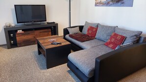 A modern living room with a grey sofa, a wooden coffee table, a TV on a black stand, and a painting of a beach scene on the wall. - Beautiful apartment in the Müritz National Park to relax and unwind or active holidays. (Federow)
