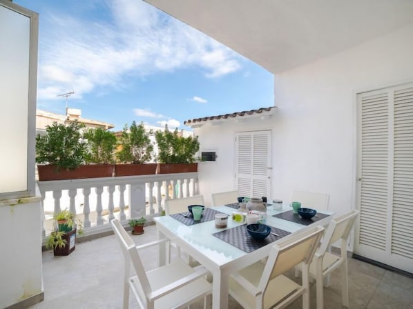 A balcony with a white table and chairs, potted plants, and a view of buildings.