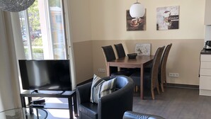 Un salon moderne avec un canapé en cuir noir, une table basse en verre et un téléviseur. On y trouve également un coin repas avec une table et des chaises.