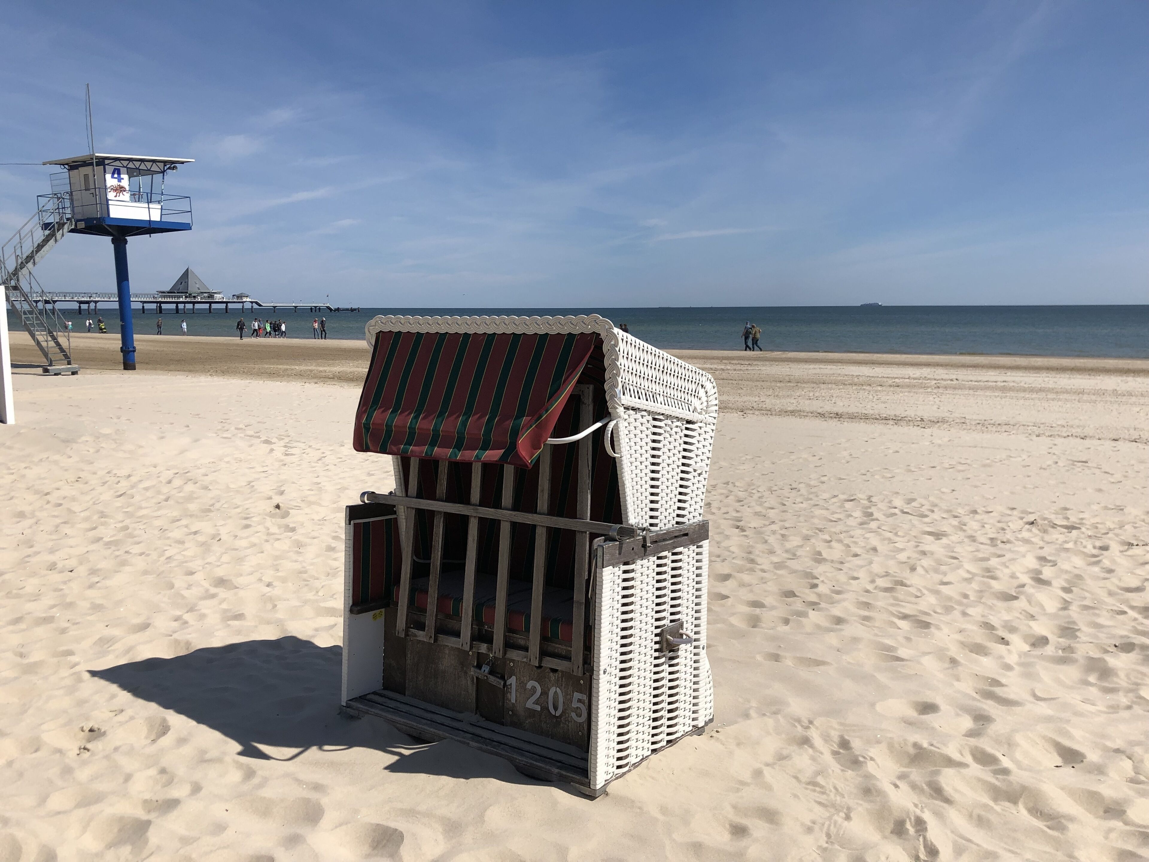 Ein Strandhäuschen mit gestreiftem Sonnensegel, der Hausnummer 120 ist sichtbar, und ein Steg im Hintergrund.