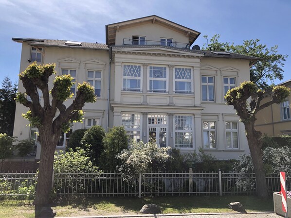 Un edificio grande de varios pisos con fachada simétrica, ventanas amplias y un balcón destacado.