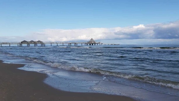Une plage avec une jetée qui s’avance dans l’océan, agrémentée de plusieurs constructions.