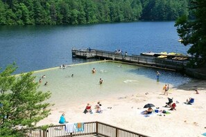 A lake with a dock, people swimming and sunbathing on the beach, and a forested area in the background. - Fox Ridge- Perfect cabin nestled in the woods with a large stacked rock firepit (Sautee Nacoochee)