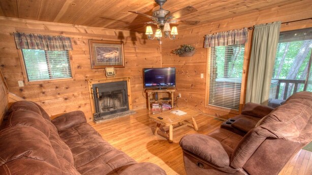 A wooden cabin interior with a fireplace, television, and leather sofas. - Fox Ridge- Perfect cabin nestled in the woods with a large stacked rock firepit (Sautee Nacoochee)