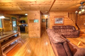 A wooden interior with a sofa, dining table, and kitchen area. - Fox Ridge- Perfect cabin nestled in the woods with a large stacked rock firepit (Sautee Nacoochee)