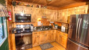 A kitchen with wooden cabinets, stainless steel appliances, a microwave, and a refrigerator. - Fox Ridge- Perfect cabin nestled in the woods with a large stacked rock firepit (Sautee Nacoochee)