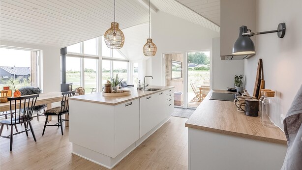 Une cuisine moderne dotée d’un îlot central, de luminaires suspendus et offrant une vue sur l’extérieur.