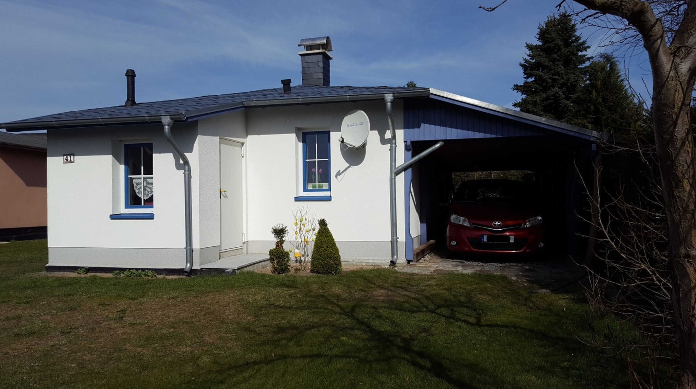A single-story house with a garage, a satellite dish, and a red car parked inside.