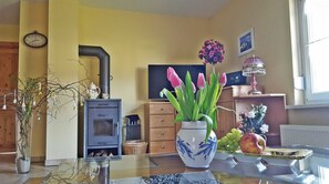 Ein Wohnzimmer mit Kamin, Fernseher, einer Uhr und einer Vase mit Blumen.