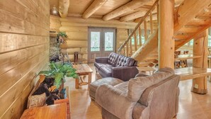 A log cabin interior with a wooden staircase, a leather sofa, and a dining area. - Ridge Views - 2BR/New Hot Tub/New Firepit/Grill/Sleeps 8 (Gatlinburg)