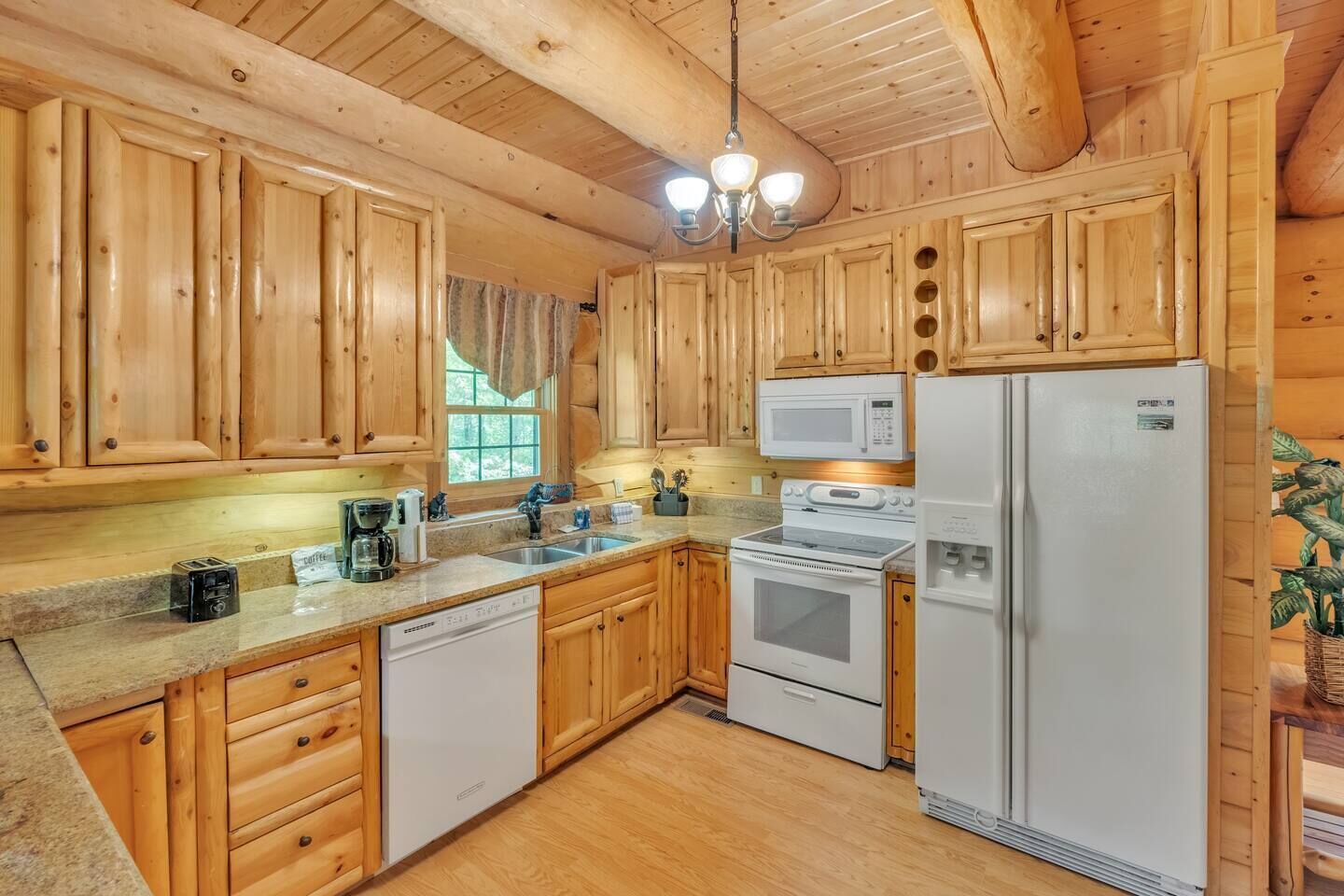 A wooden cabin-style kitchen with a sink, stove, microwave, and refrigerator.
