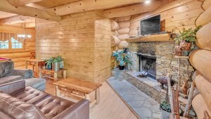 A log cabin interior with a stone fireplace, wooden furniture, and potted plants. - Ridge Views - 2BR/New Hot Tub/New Firepit/Grill/Sleeps 8 (Gatlinburg)