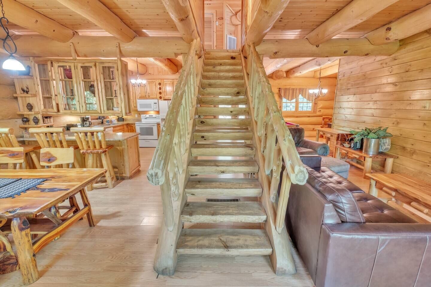 Una escalera de madera conduce a un área de entrepiso con una mesa de comedor y sillas, un sofá y una cocina al fondo.