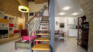 Un espacio habitable en varios niveles con una escalera, estanterías abiertas, una zona de comedor y una cocina.