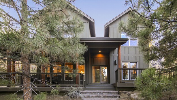 A modern two-story house with a stone staircase leading to the entrance, surrounded by pine trees.