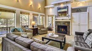 A spacious living room with a fireplace, comfortable seating, large windows, and a view of the outdoors.