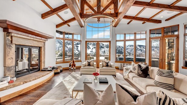 Un ampio soggiorno con camino, grandi finestre e un soffitto alto con travi a vista.