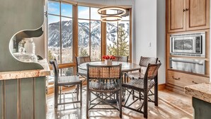Una cucina con un tavolo da pranzo, sedie in vimini, forno a incasso e vista sulle montagne innevate.