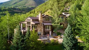 Un'ampia casa in pietra, su più piani, circondata da una fitta foresta, con una montagna sullo sfondo.