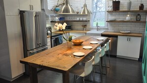 A modern kitchen with white cabinets, stainless steel appliances, and a wooden dining table with chairs. - Charming Carriage House in Niagara's Wine Country (Niagara Falls)
