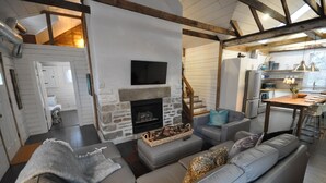A modern living room with a stone fireplace, grey sofas, and a wooden staircase. - Charming Carriage House in Niagara's Wine Country (Niagara Falls)