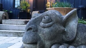 A stone sculpture of a sleeping animal in front of a dark wooden house with a porch and potted plants. - Charming Carriage House in Niagara's Wine Country (Niagara Falls)