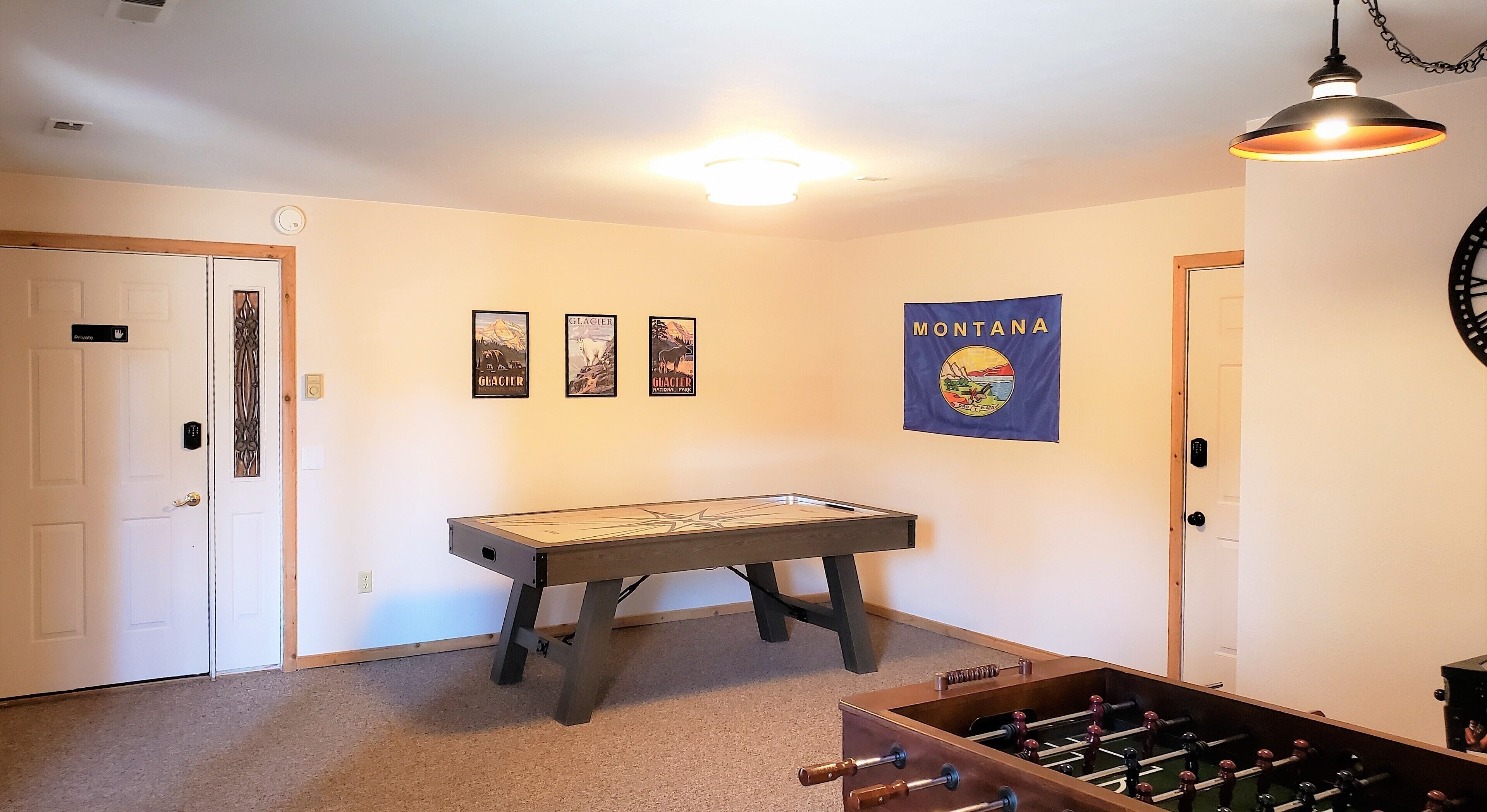 A room with a foosball table, a private door, and a wall with a Montana flag and three framed pictures.