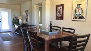 Un comedor con una mesa y sillas de madera, una botella de vino y un cartel enmarcado en la pared.