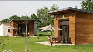 Une cabane moderne en bois dotée d’un patio comprenant une table et des chaises, le tout entouré d’une pelouse bien entretenue.