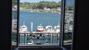 Blick aus einem Fenster auf einen Hafen mit Booten, einem Leuchtturm und Gebäuden am Hang.