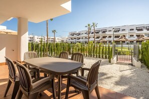 A patio area with a table and chairs, a view of a building complex in the background, and a pathway leading to a gated entrance. - Apartamento Palmera (Mar de Pulpi) (San Juan de los terreros)
