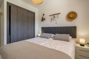 A bedroom with a large bed, a wardrobe, a bedside table with a lamp, and wall decorations including a hat and jewelry. - Apartamento Palmera (Mar de Pulpi) (San Juan de los terreros)