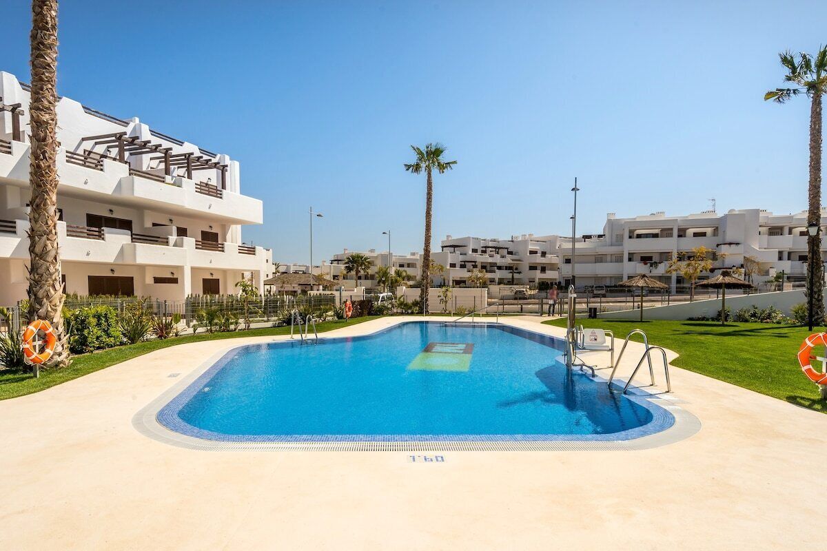 Una piscina rodeada de palmeras y un edificio blanco con balcones.