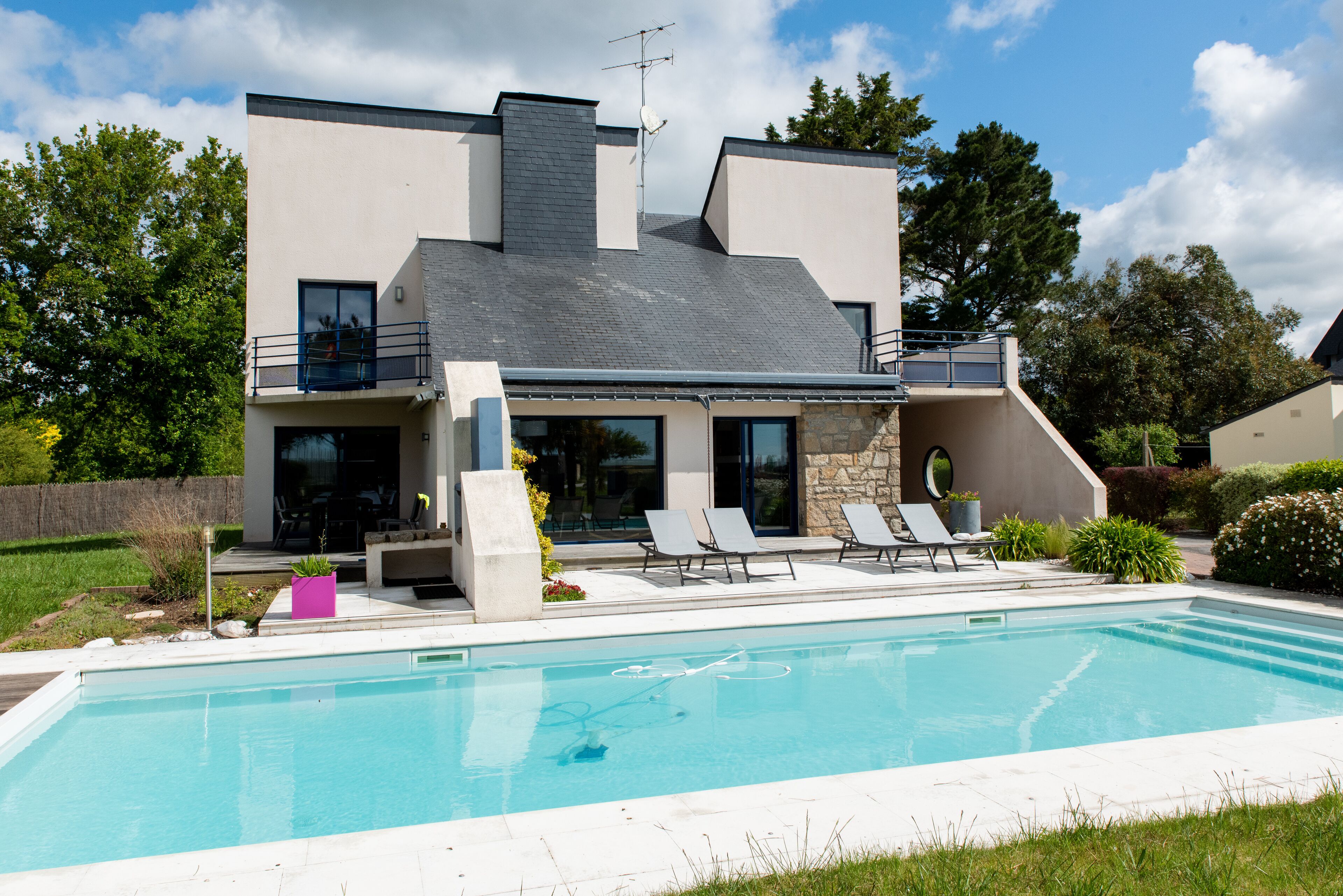 A modern two-story house with a swimming pool, outdoor seating, and a stone facade.