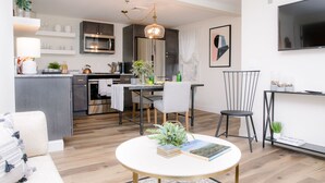Una cucina moderna con angolo pranzo, un soggiorno con divano e una TV a parete.