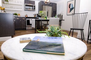 A modern kitchen with dark cabinets, a marble countertop, and a dining area with a round table. - Historical  Downtown 1bedroom (Lenox)