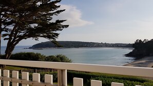 A coastal view from a balcony with a railing, overlooking a calm sea, a small island, and a distant town.